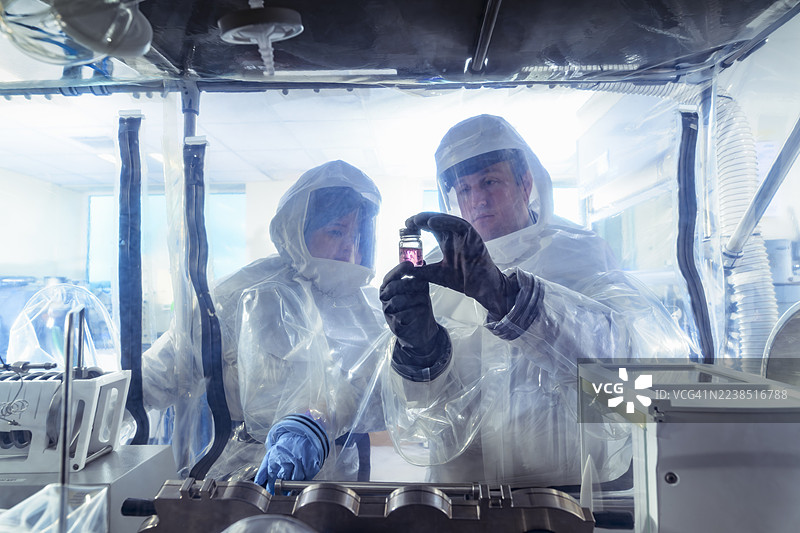 科学家在隔离手套箱中工作，在实验性水晶实验室中检查溶液瓶。图片素材