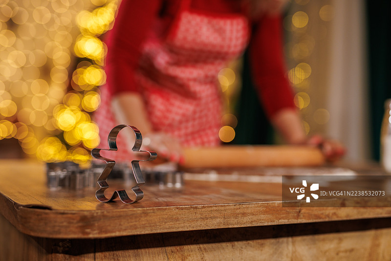 姜饼人饼干模具放在木桌上，背景有擀面杖和圣诞彩灯。图片素材