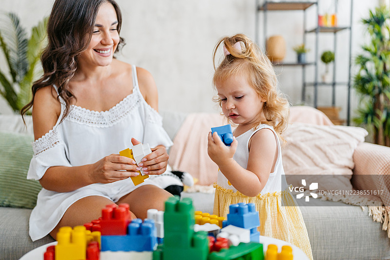 年轻的母亲和女儿在客厅玩积木玩具图片素材