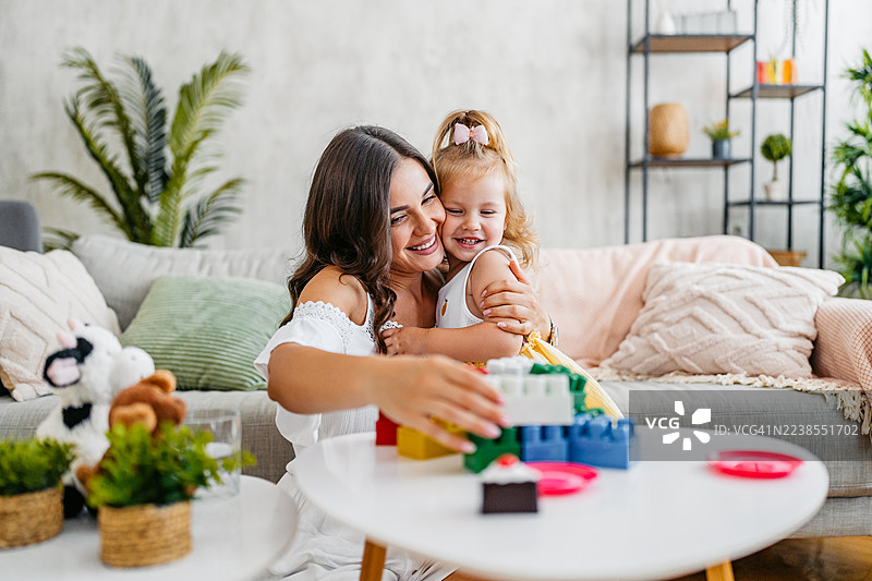 年轻的母亲和女儿在客厅玩积木玩具图片素材