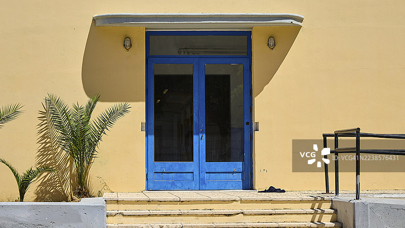 希腊拉科斯莱罗斯岛多多塞群岛波尔托拉戈的一座黄色建筑的蓝色入口,旁边有植物,历史主义,装饰艺术,理性主义,波尔托拉戈,拉科斯,莱罗斯,佐泽卡尼西亚群岛,希腊群岛,希腊图片素材
