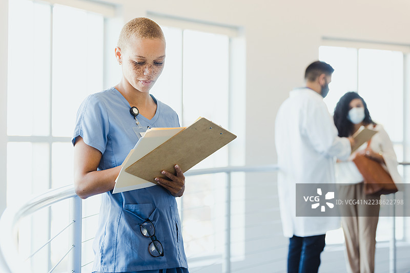 医务人员在同事们在旁边交谈时查阅图表。图片素材