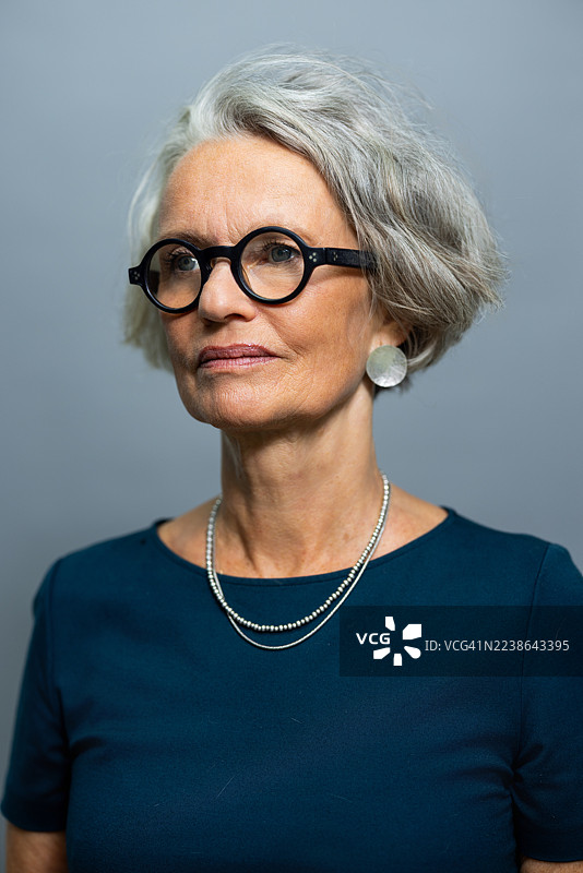 一位年长的女性背对着镜头，站立在灰色背景前。图片素材