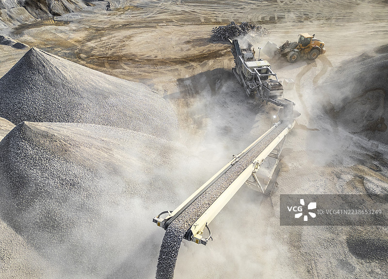 尘土飞扬的户外环境中，拥有重型机械和输送带系统的工业砾石采石场图片素材