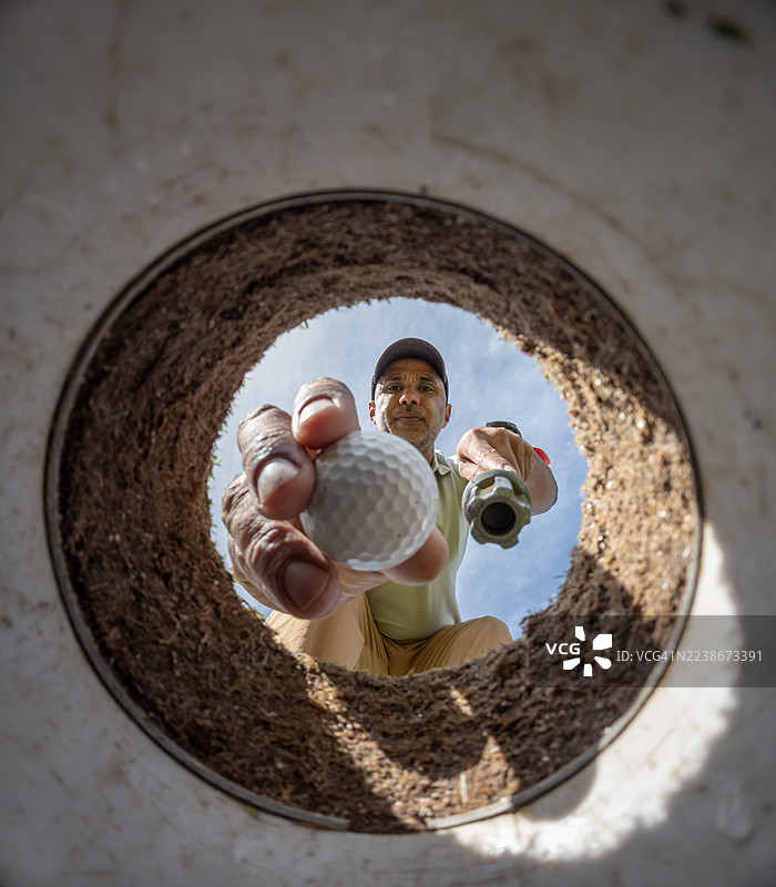 第一人称视角，一名男子将高尔夫球从洞中取出图片素材