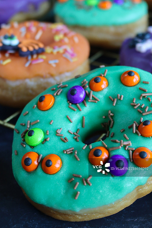 万圣节主题糖霜甜点的全画幅图像，有紫色、橙色和绿色糖霜甜甜圈，带有鬼鬼祟祟的眼睛、骨头、骷髅和蜘蛛装饰，黑色大理石纹背景，前景清晰。图片素材