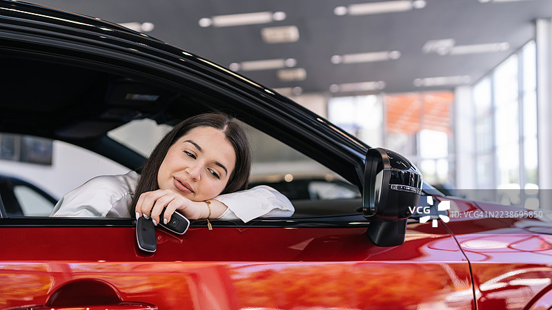 年轻女子在经销商处坐在新车里，手持车钥匙，面带微笑。图片素材