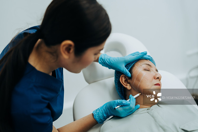 诊所里，整形外科医生正在为一位中年女性的面部进行美容手术标记，准备进行面部提升手术。图片素材