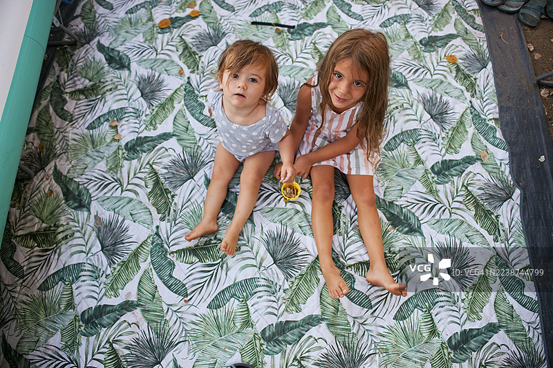 几个时髦的年轻女孩赤脚坐在有热带叶子图案的垫子上，在室内拿着一个小黄碗。图片素材