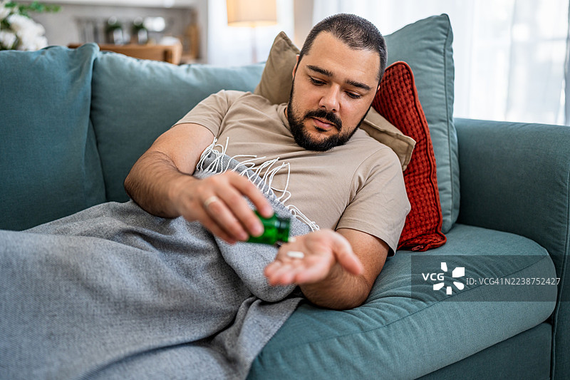 生病的男人在家里的沙发上吃药图片素材