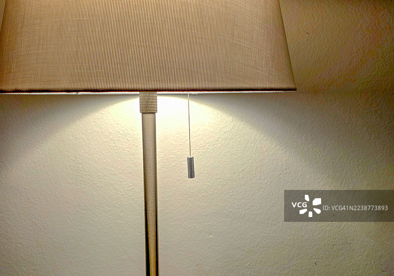 现代落地灯，米色灯罩配金属拉链，在纹理墙壁上散发柔和光芒——温馨、简约的室内细节，唤起舒适感、简洁性和现代家居设计的实用优雅。图片素材