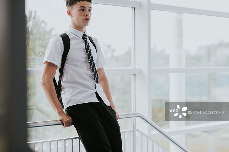 一个高中男生穿着未束进裤子的衬衫，倚靠在学校走廊的栏杆上，表情空白。概念图，留有复制空间。图片素材