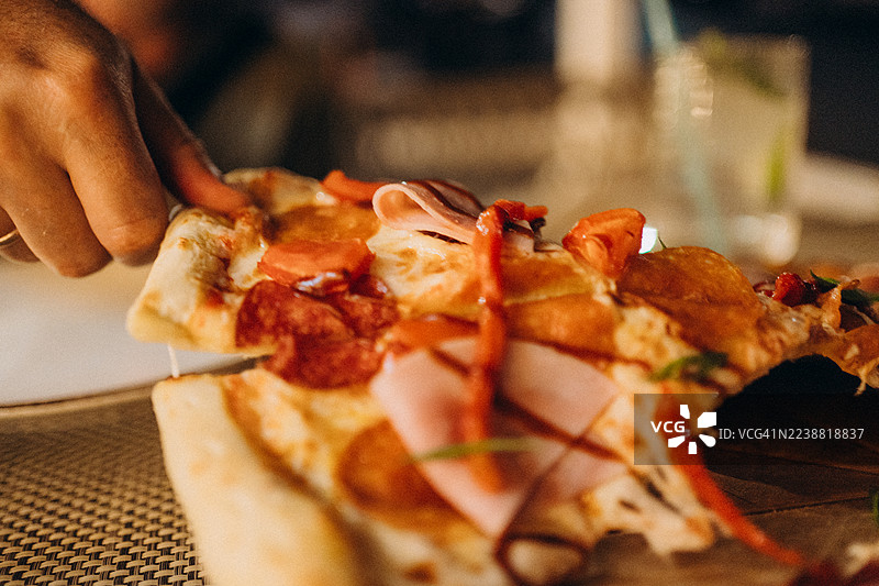 手递披萨片，上面有意大利辣香肠和火腿图片素材