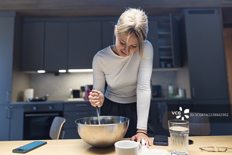 快乐的年轻女子在舒适的现代厨房里搅拌面糊图片素材