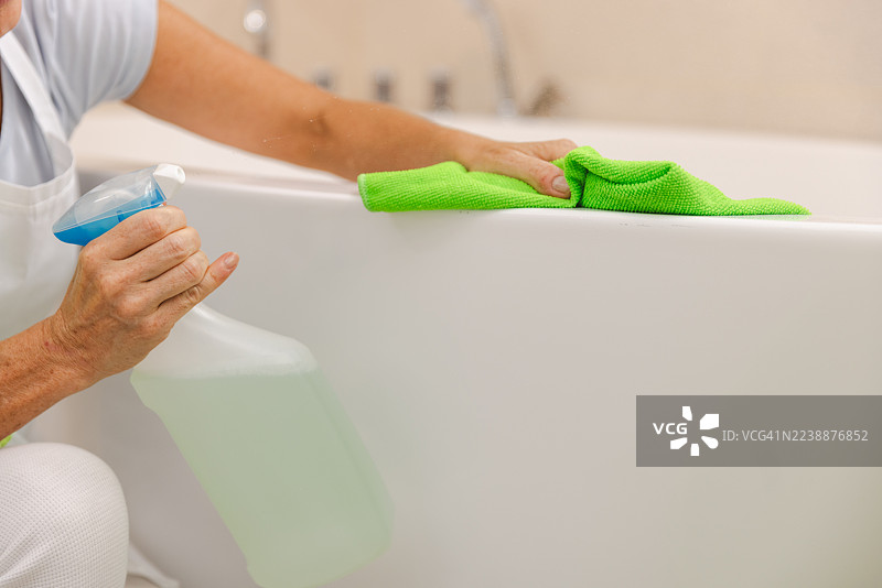 明亮浴室里的人用喷壶和绿色抹布清洁浴缸图片素材