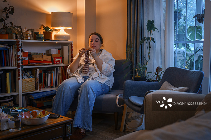 一位女士晚上在家舒适地躺在沙发上织毛衣图片素材