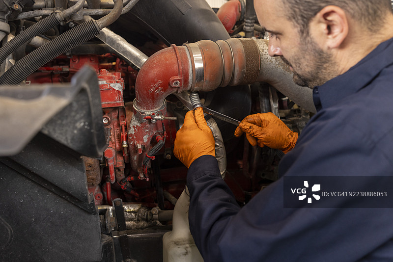 身着蓝色制服的男性机械师正在使用工具修理红色卡车的发动机图片素材