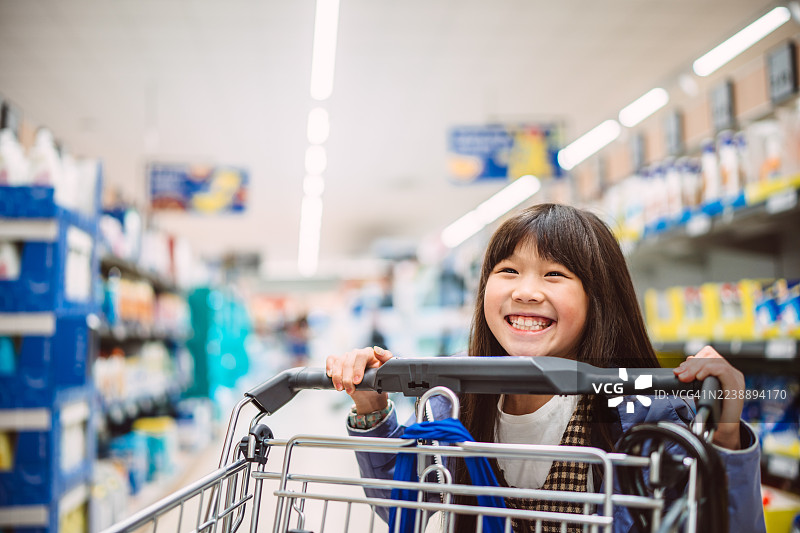 购物车的微笑女孩在超市过道里图片素材