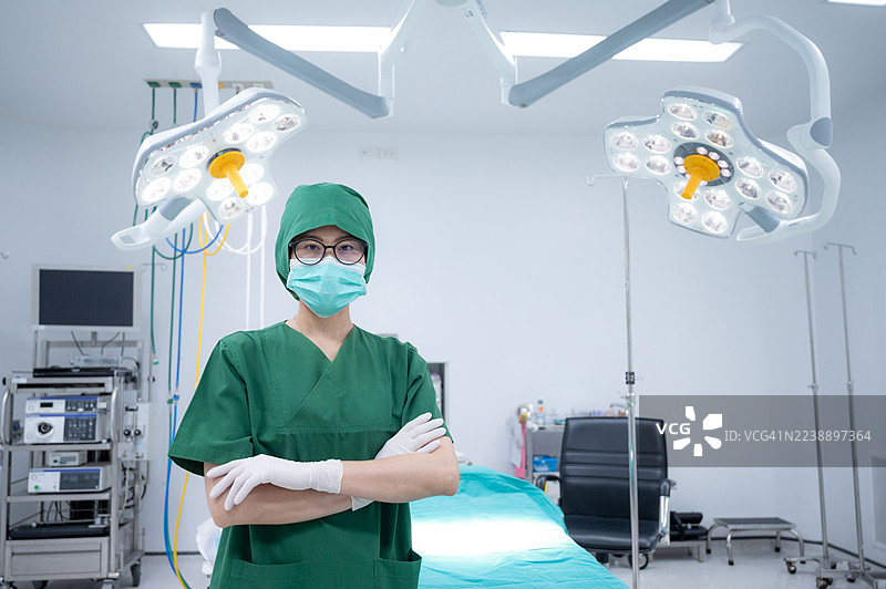 亚洲的医护人员身穿手术服，双手交叉站在手术室里工作。图片素材