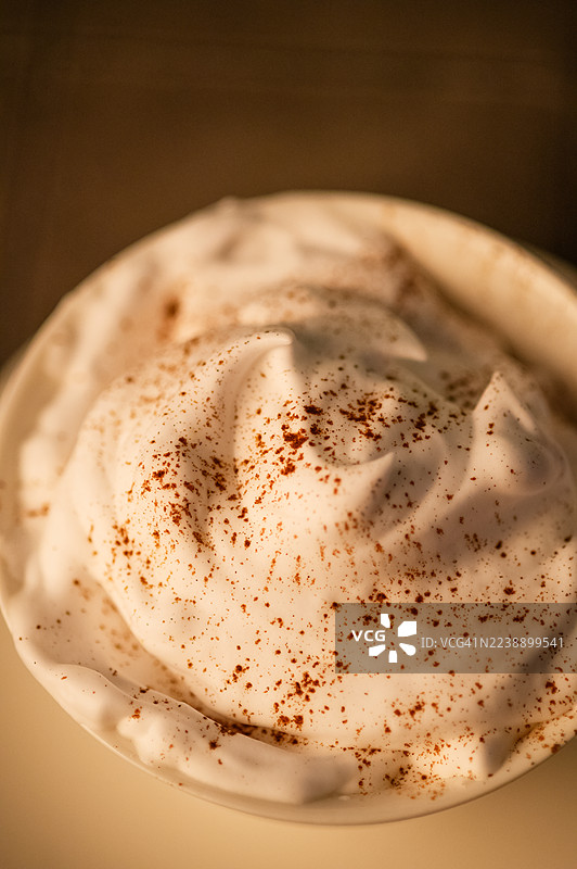 温暖光线下，肉桂粉撒在鲜奶油上的特写图片素材