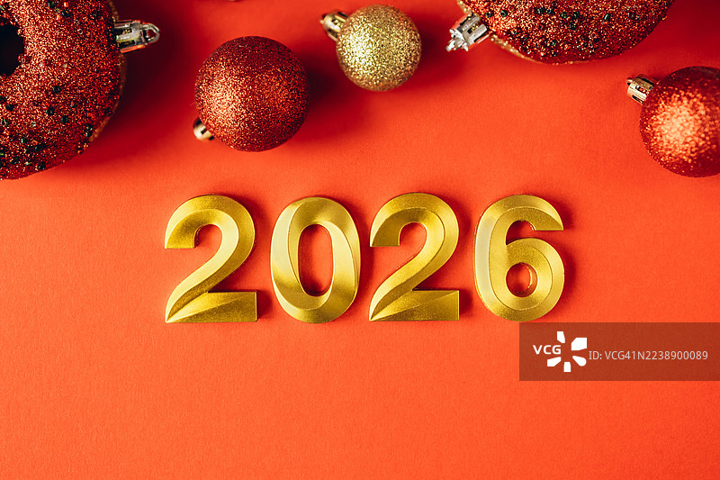 明亮的红色背景上，闪耀的金色“2026”数字环绕着闪闪发光的红金色圣诞彩球。节日新年和假日庆祝概念图片素材