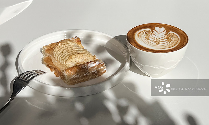 阳光明媚的周日，在当地小咖啡馆里，刚出炉的苹果卷配上拉花卡布奇诺，享受悠闲时光。图片素材