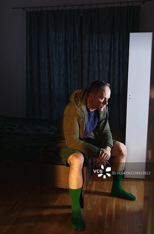 身穿绿色夹克和绿色袜子，男子坐在床边图片素材