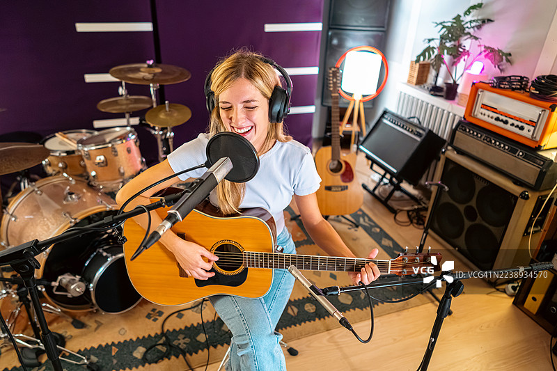 一位女音乐家在舒适的录音室里，在现场声音检查和录音时弹奏木吉他。图片素材