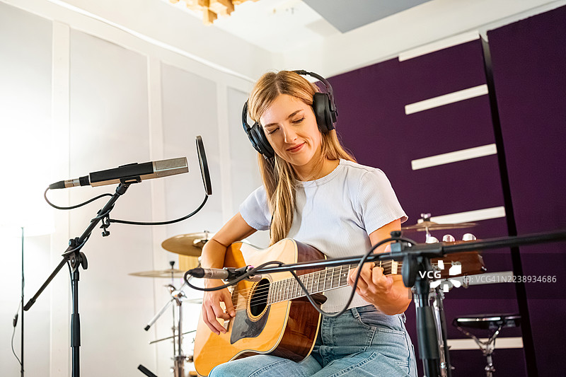 一位女性吉他手在录音室进行声音检查，她戴着耳机，手持一把原声吉他。图片素材