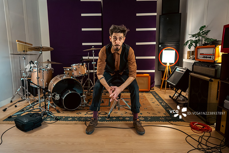 一位专注的音乐家坐在家庭录音室中，身后是鼓和放大器。图片素材