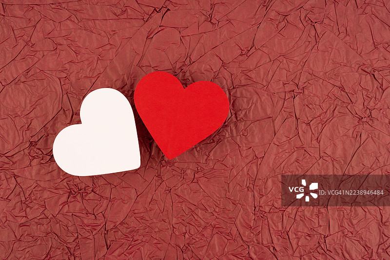 白色和红色的纸心在红色揉皱的纸张背景上，留有复制空间的位置。图片素材