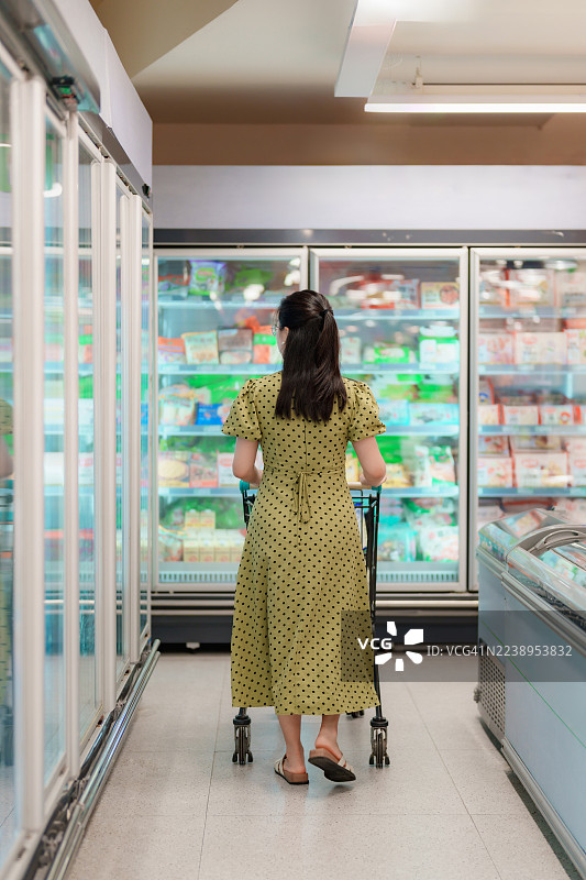 一名亚洲女性在超市冷藏区挑选商品图片素材