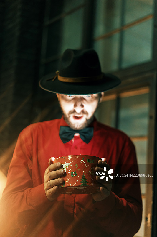 身穿红衣戴帽的神秘男子展示着节日圣诞饼干罐图片素材