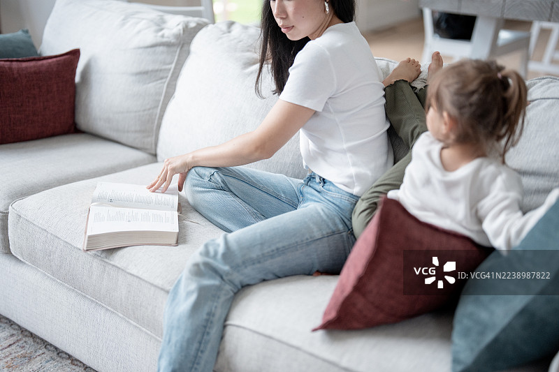 亚洲妈妈在家温馨的客厅沙发上和女儿一起读书图片素材