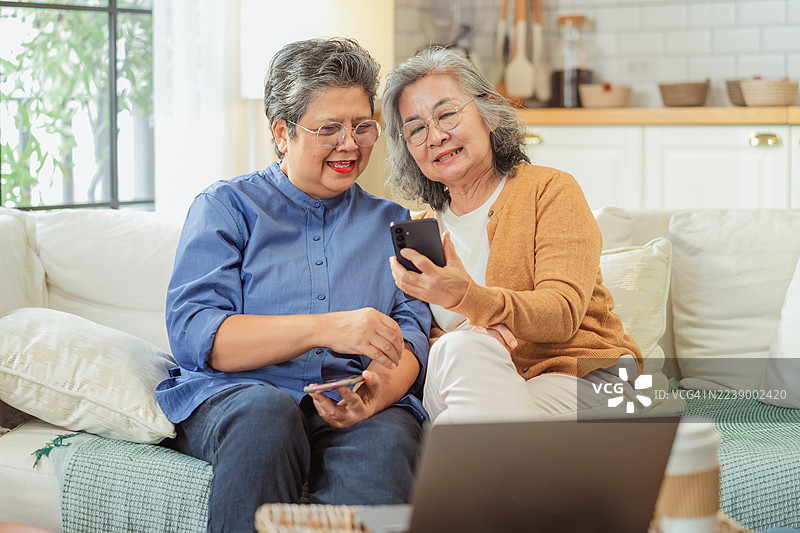 一位亚洲退休老妇人及其朋友在家中使用人工智能金融助手，规划养老金、保险和储蓄策略，学习智能聊天机器人技术，以实现个人投资、退休目标和未来稳定。图片素材