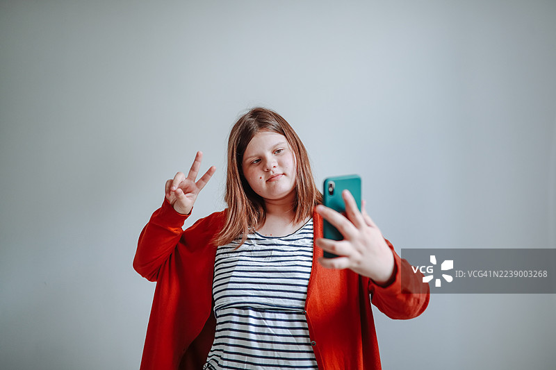 一个胖乎乎的十几岁的孩子，靠着一栋房子的白墙，手里拿着手机。图片素材