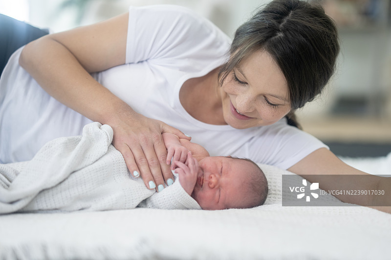温馨的新生儿与慈母的亲密时刻，在家中白色毯子上休憩，图片素材