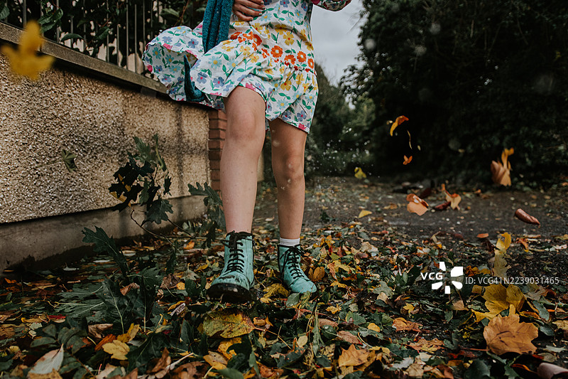 下雨天，一个孩子在堆积如山的落叶中跳跃。图片素材