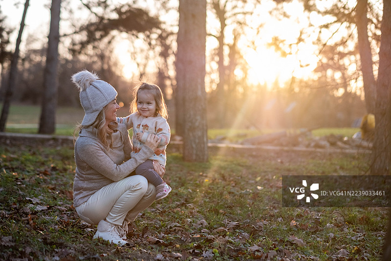 秋日公园夕阳下，母亲抱着孩子开怀大笑图片素材