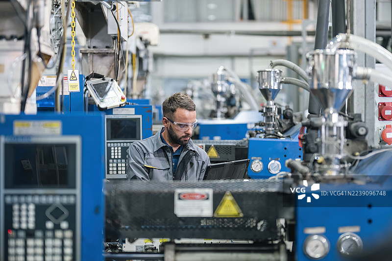技术人员在工厂工作，他正在进行日常例行工作，检查塑料注塑机的控制面板。图片素材