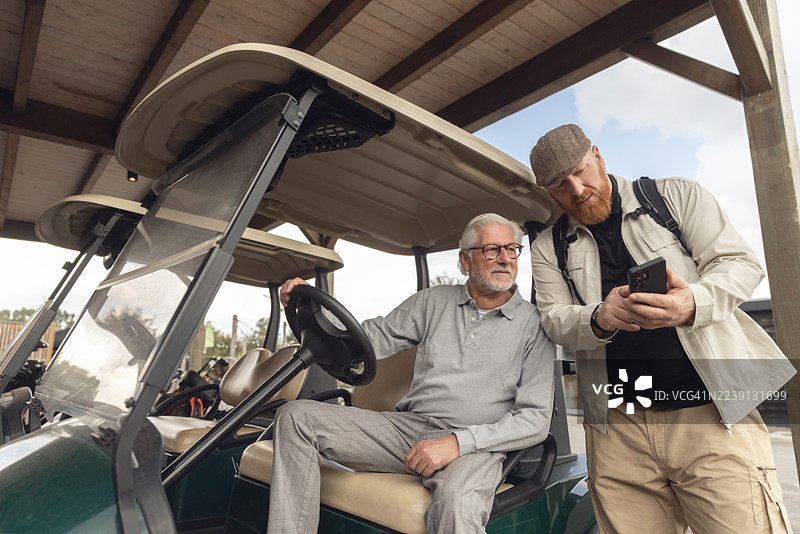 欧洲，一位退休老人与球童在自己的高尔夫球车上打高尔夫球。图片素材