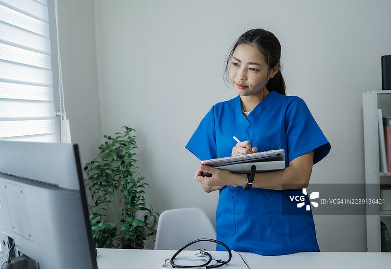 护士在医院办公室使用平板电脑管理病人，并与朋友交流。图片素材