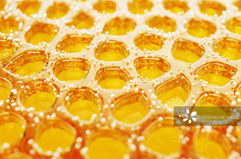 黄色背景上由蜂蜜制成的抽象蜂窝形状，带有气泡。图片素材