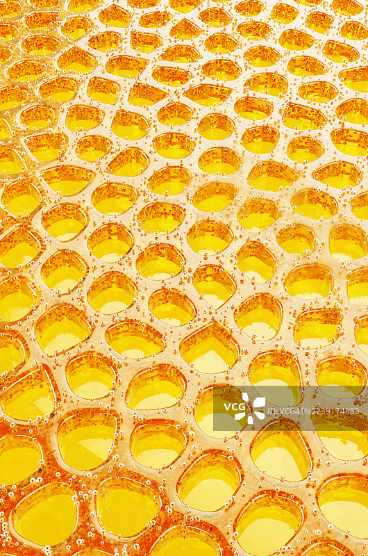 黄色背景上由蜂蜜和气泡组成的抽象蜂窝形状。图片素材