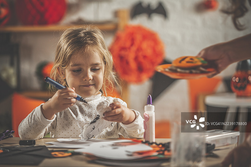 小女孩在家用马克笔和胶水制作万圣节装饰品，绘制南瓜笑脸图片素材