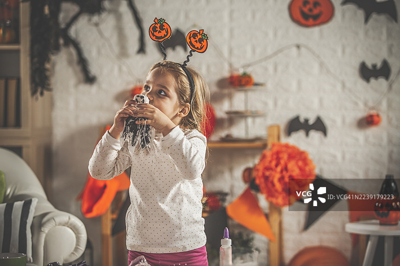 戴着南瓜头饰的小女孩在充满万圣节装饰和手工艺品的派对上玩耍图片素材
