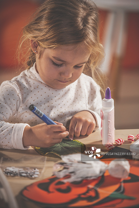 小女孩在桌边用马克笔、胶水和树叶手工材料进行创作和绘画图片素材