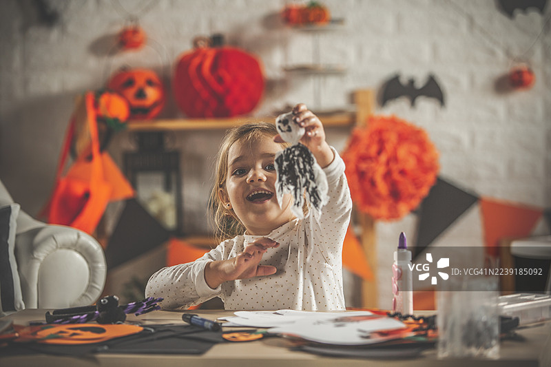 快乐的小女孩在摆满南瓜和蝙蝠的节日桌旁制作万圣节装饰品图片素材