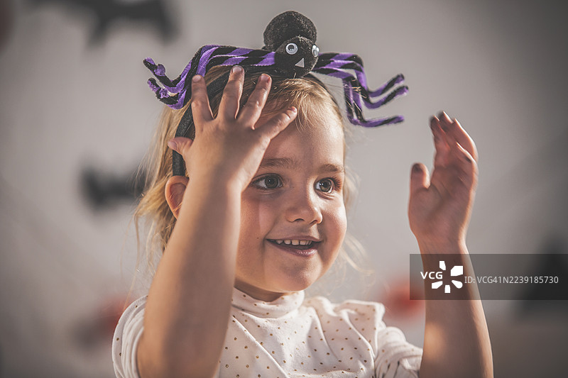 戴着紫色蜘蛛头饰的小女孩在节日气氛中举起双手微笑图片素材