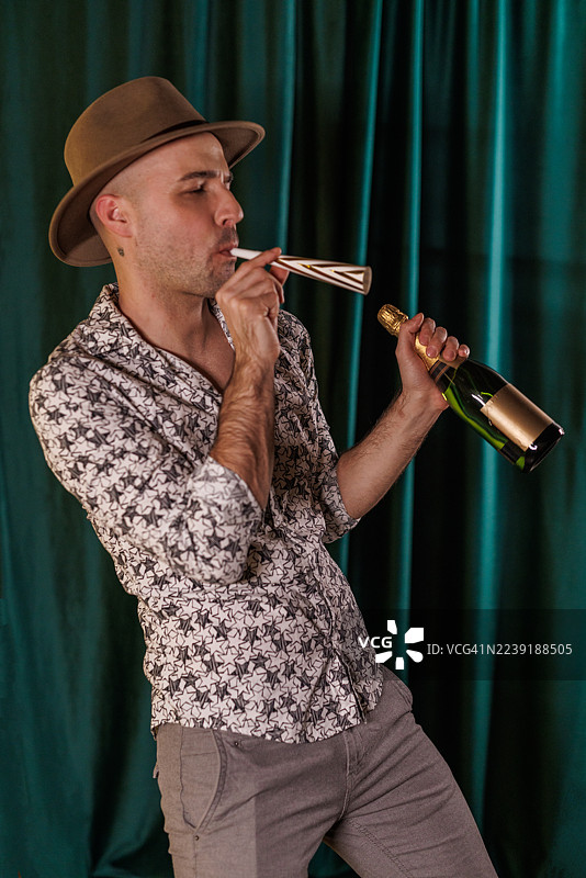 身穿印花衬衫和帽子的男人在绿色幕布背景前手持香槟庆祝图片素材